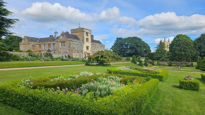 A long distance view of canons Ashby House and the Priory Church with the formal gardens in bloom for summer including hedges and mixed colours